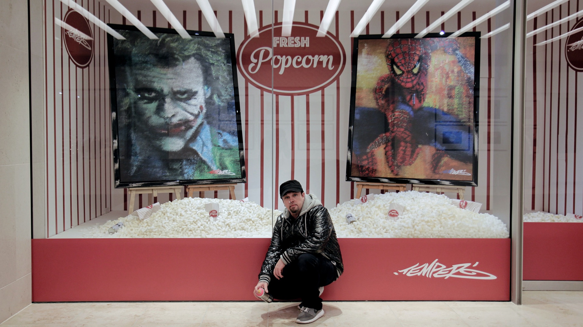Shop window installation with Joker and Spider-Man portraits above a bed of popcorn, under a ‘Fresh Popcorn’ sign