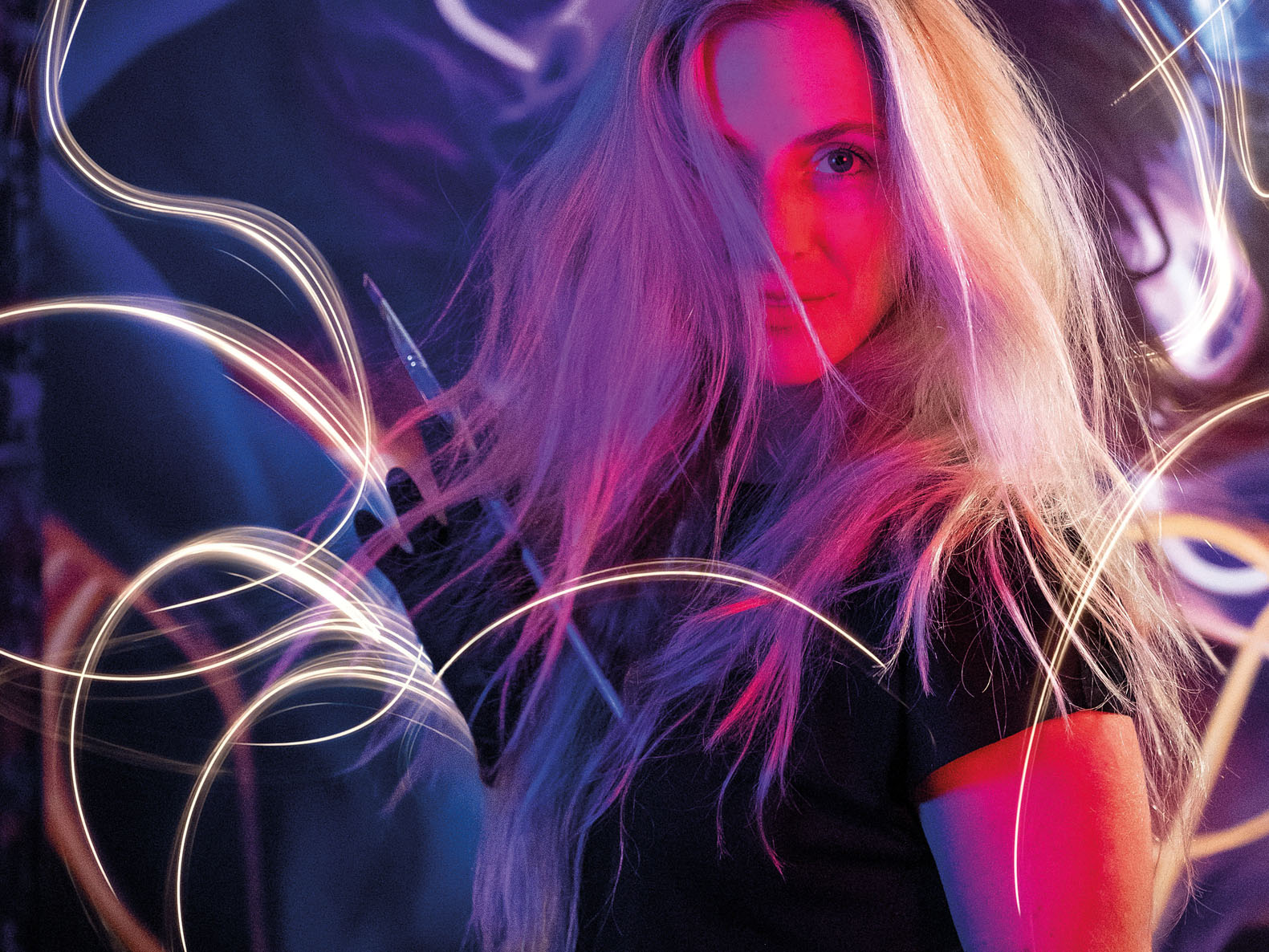 A portrait lit in pink and blue, surrounded by trails of light