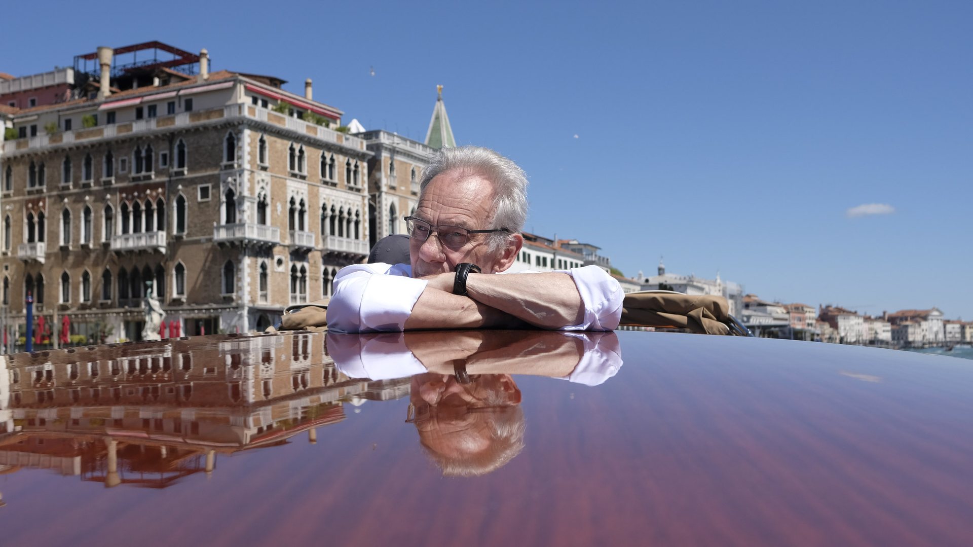 John Myatt resting his arms on the polished roof of a boat in Venice, with the Grand Canal behind him