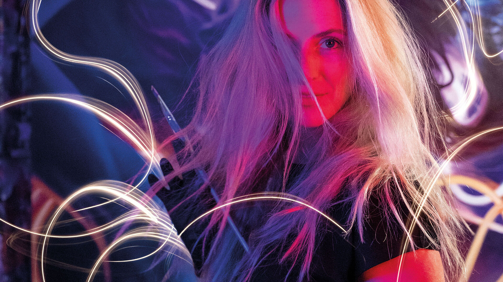 A portrait lit in pink and blue, surrounded by trails of light