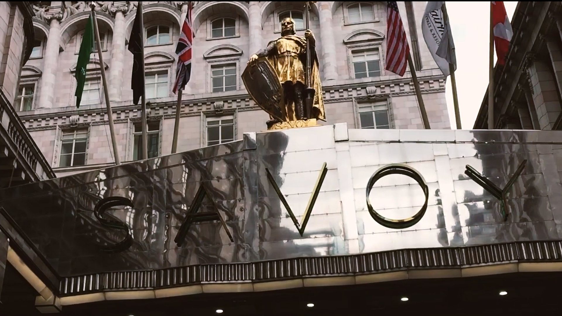 The Savoy hotel sign beneath a golden statue and flags